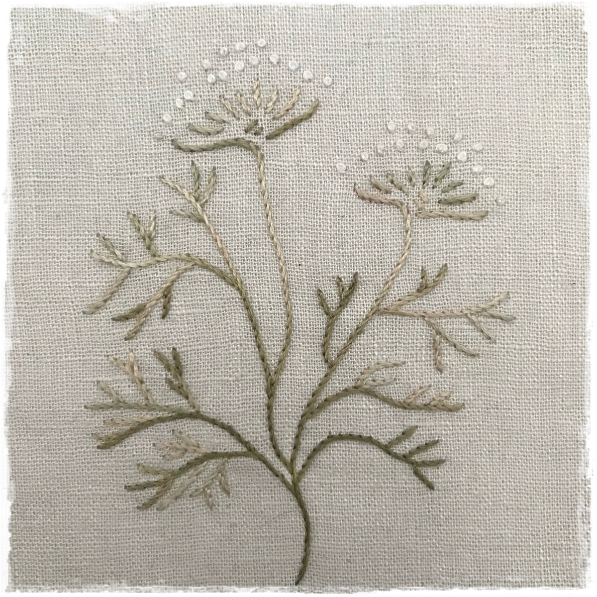 needlecraft pattern featuring a floral design with beige and white colors on a linen background