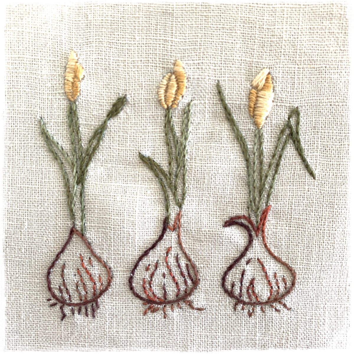 linen quilt fabric with three hand-stitched tulip designs in different shades of green and red