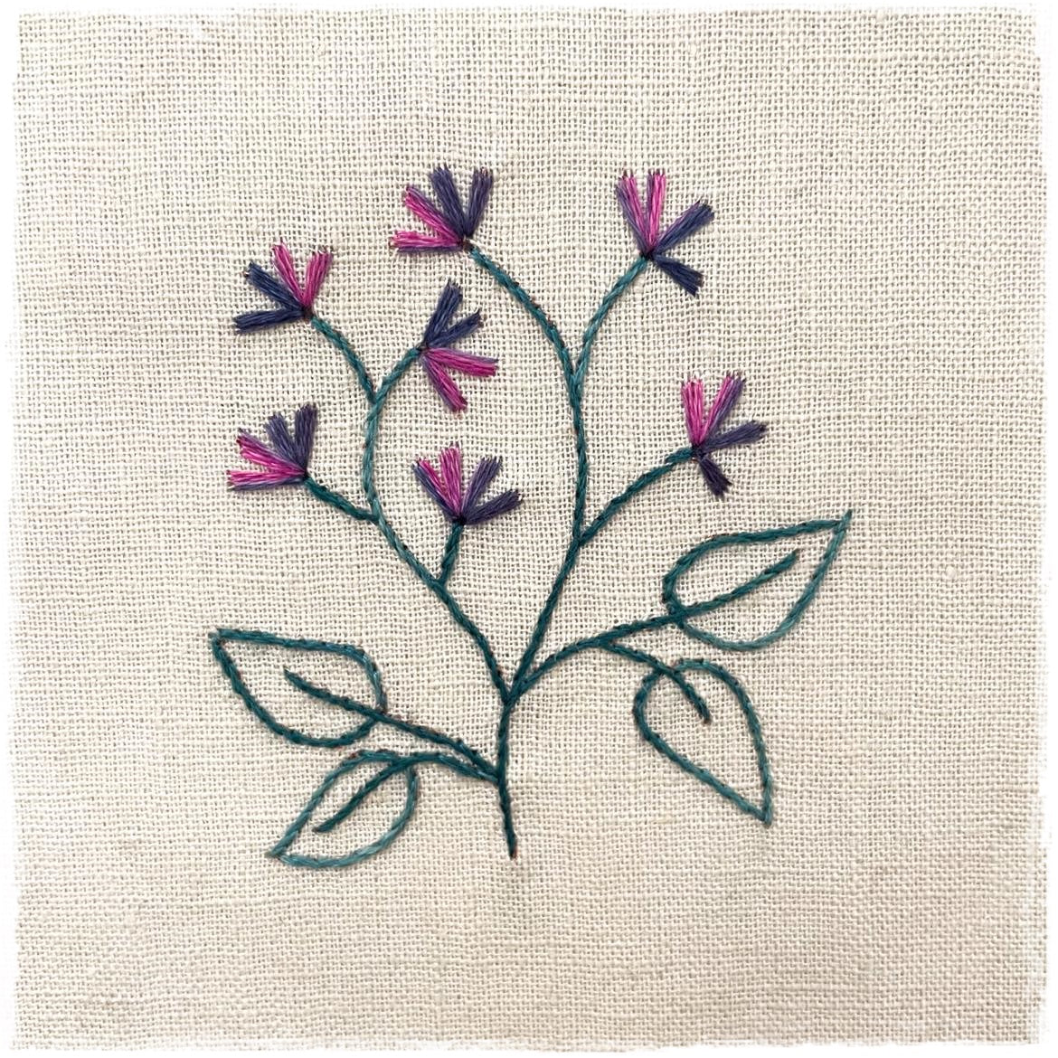 needlecraft pattern for a floral design, featuring a trace off design with color instructions and a sample stitched on a linen background