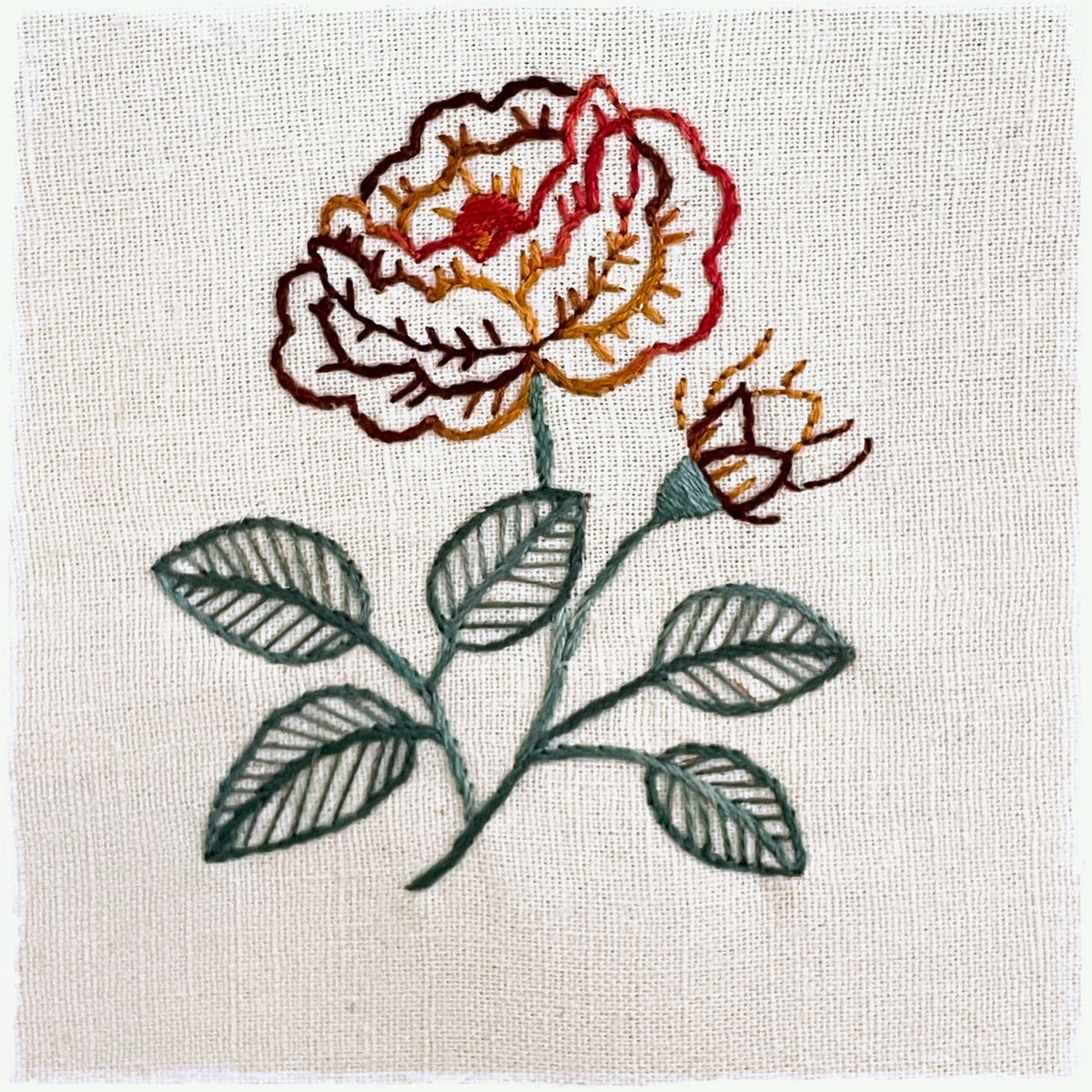 needlecraft pattern featuring an embroidered design of a flower and leaves on a linen background.