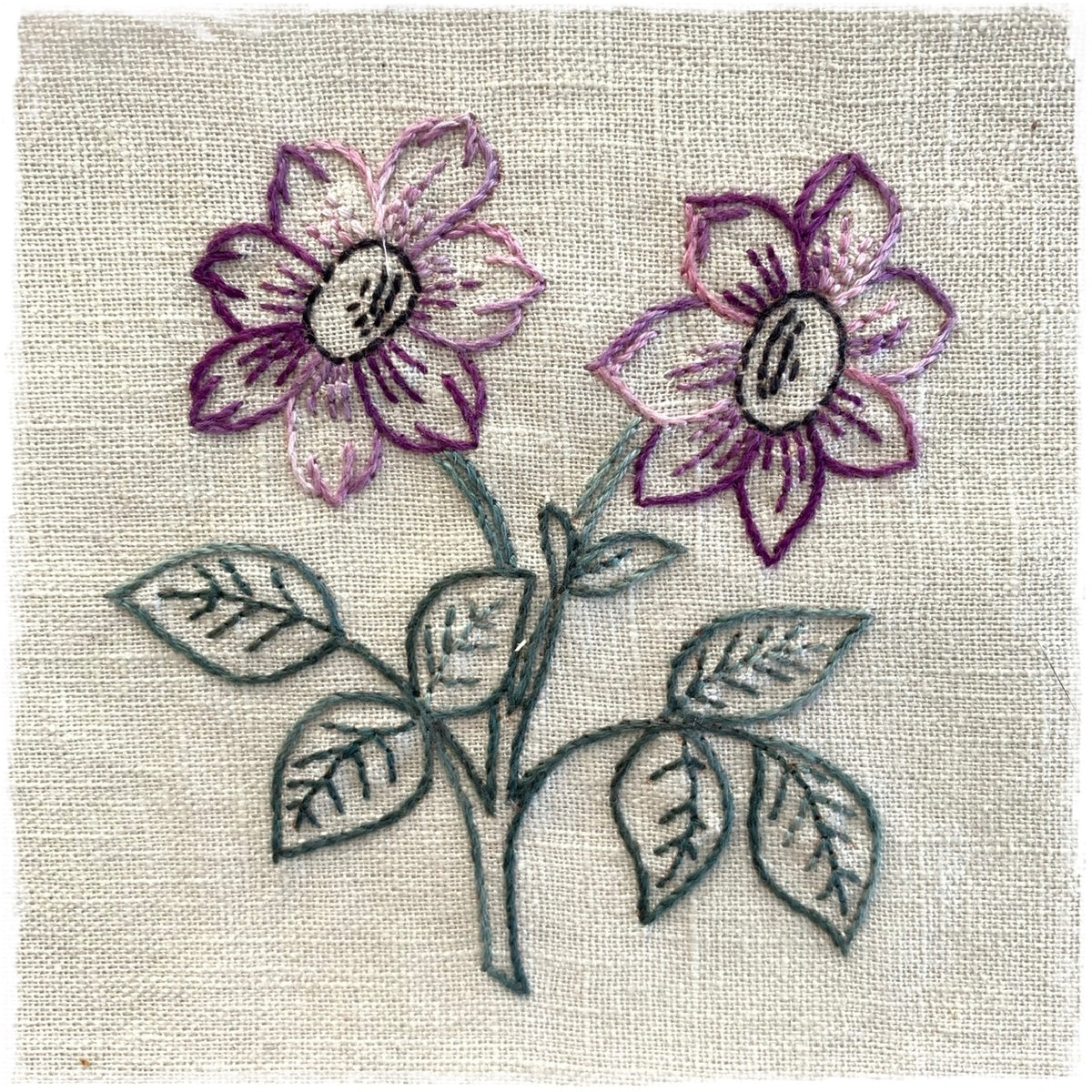 quilted fabric with a floral design, featuring a purple and white flower and green leaves on a beige background.