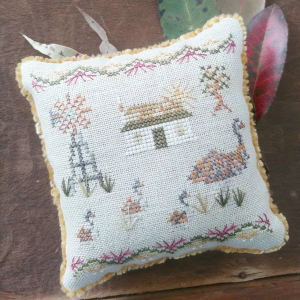 Embroidered pillow with a mother Emu and chicks, an Australian farmhouse and windmill design on a wooden surface.