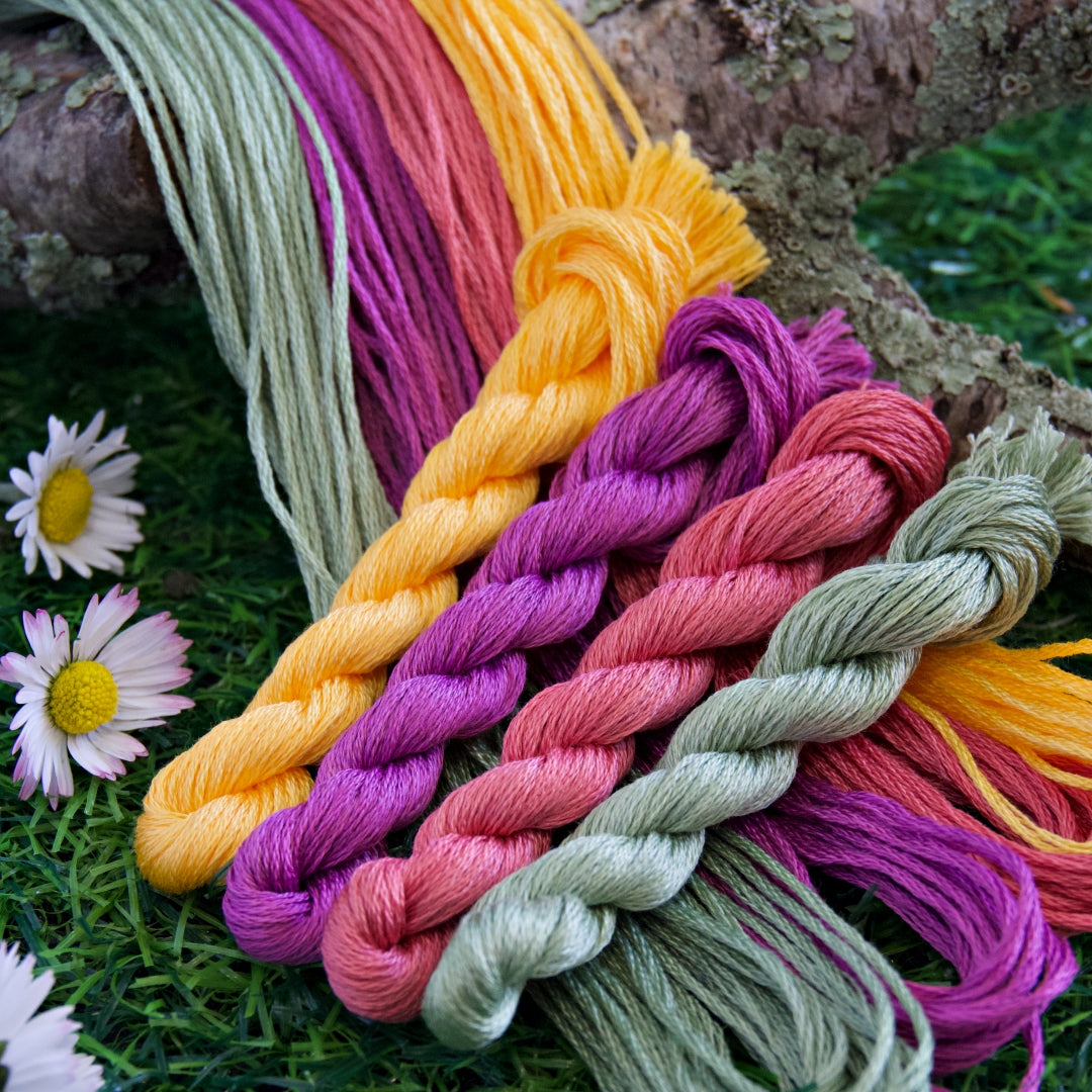 Four skeins of spring themed embroidery threads. The thread colours are pale sage green, bright yellow, magenta, and coral pink.