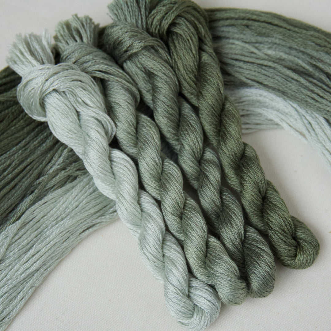 Four twisted embroidery skeins in a gradient pack of grey-green from pale icy to dark moody tones.