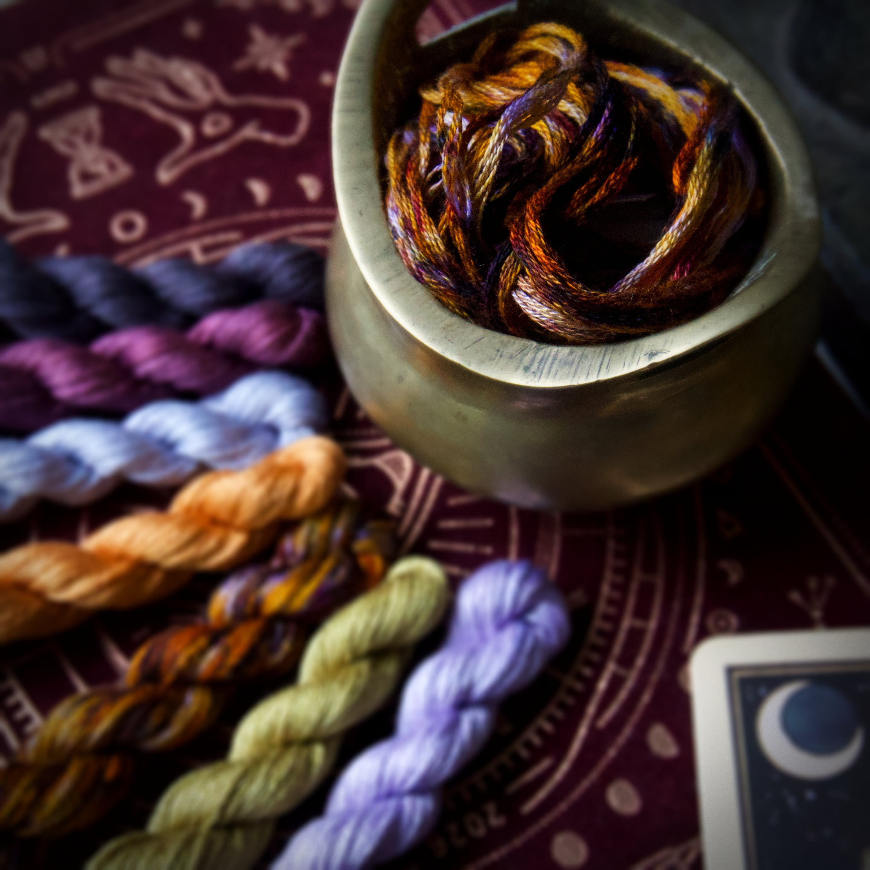 Seven twisted and one untwisted  embroidery threads in blue, green, purple, vermilion and orange.
