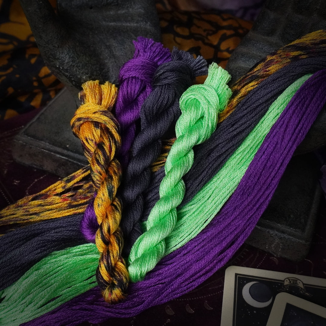 Four twisted embroidery threads in lime green, charcoal grey, vibrant purple and burnt orange.