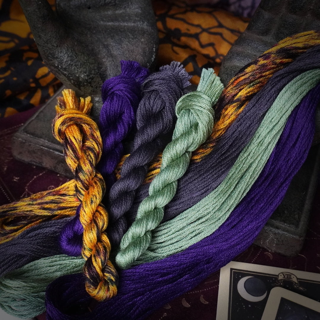 Four twisted embroidery threads in burnt orange, grey, bright purple and dusty green.