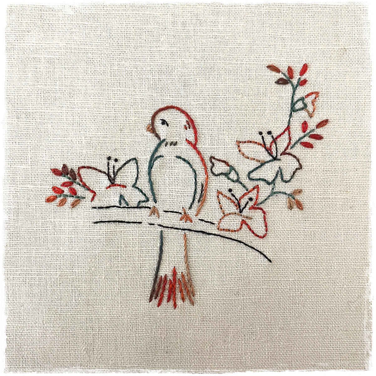 needlecraft pattern featuring an embroidered design of a bird on a branch with accompanying floral elements, stitched on a linen fabric.