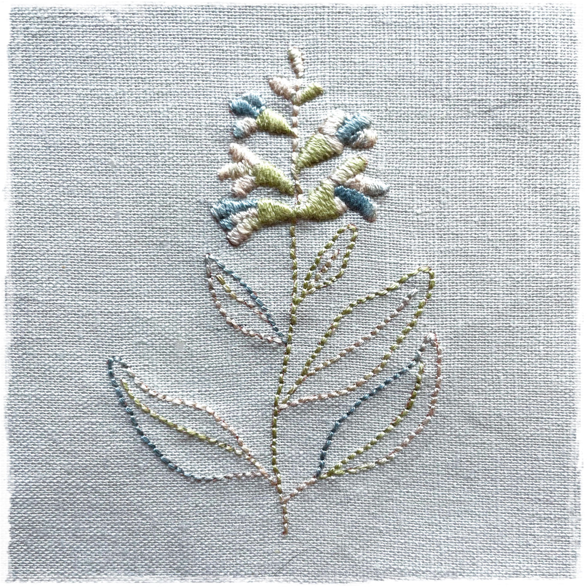 needlecraft canvas with a floral design, stitched in colors resembling blue, green, and white, on a light background.