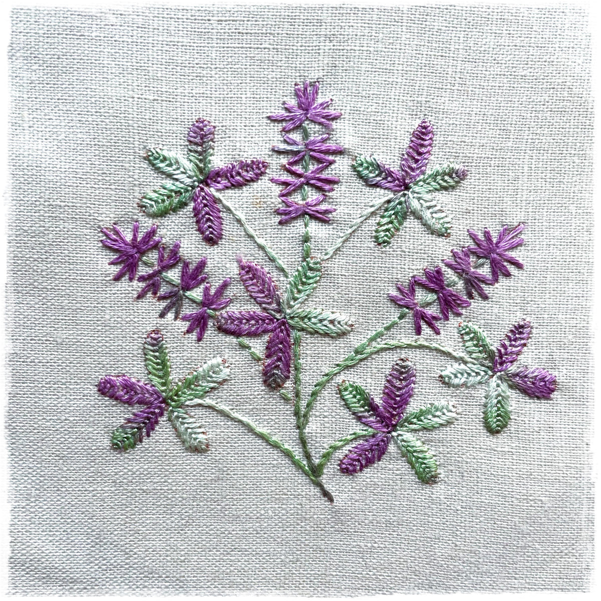 quilted journal page with a floral design, primarily in purple and green, stitched on a white background.