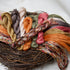 A close-up of multiple skeins of twisted embroidery floss in autumn harvest colours arranged on a rustic woven nest base against a soft white background.