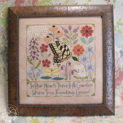 Framed cross-stitched artwork with flowers and a butterfly on a pink background.