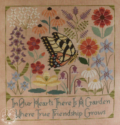 A square cross-stitch sampler featuring a yellow and black swallowtail butterfly surrounded by colorful wildflowers on a beige fabric background, with the embroidered text &