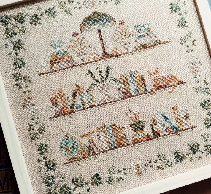 Mojostitches cross-stitch of 3 shelves with books plants lamp various things