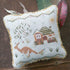 Decorative pillow with cross-stitched design of a federation style house and kangaroo on a wooden surface.