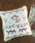 Decorative pillow with cross-stitched design featuring animals and a quiet campsite by a creek on a wooden surface.