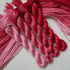 Four skeins of embroidery floss in a vertical gradient of shades from light pastel pink to deep crimson red, arranged on a light gray background.