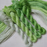 Four twisted skeins of embroidery thread in shades of grassy green through to pale mint, arranged on a light fabric background.