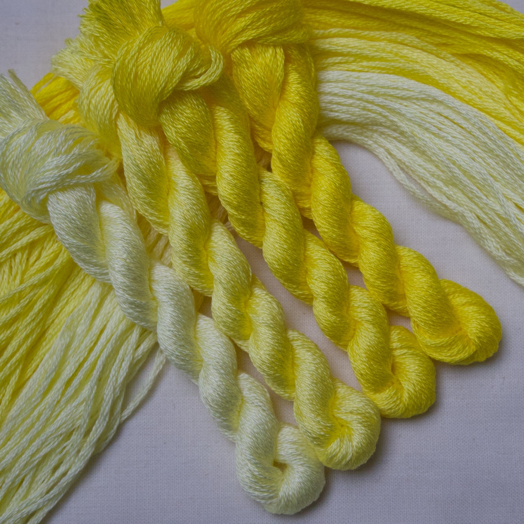 Bright yellow and pale lemon embroidery thread twisted into braids, arranged on a light fabric background.