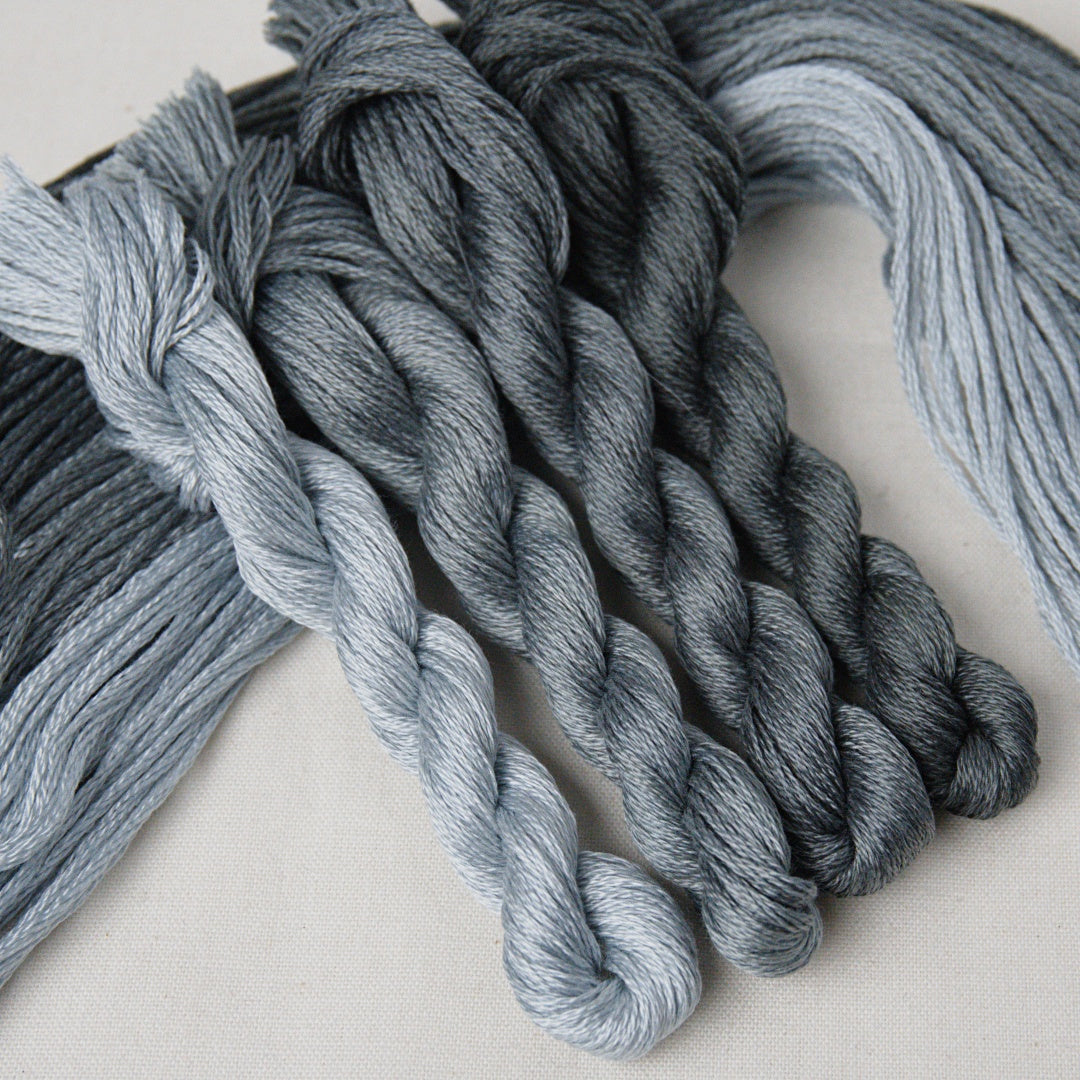 Several twisted skeins of yarn in soft blue-grey and charcoal tones.