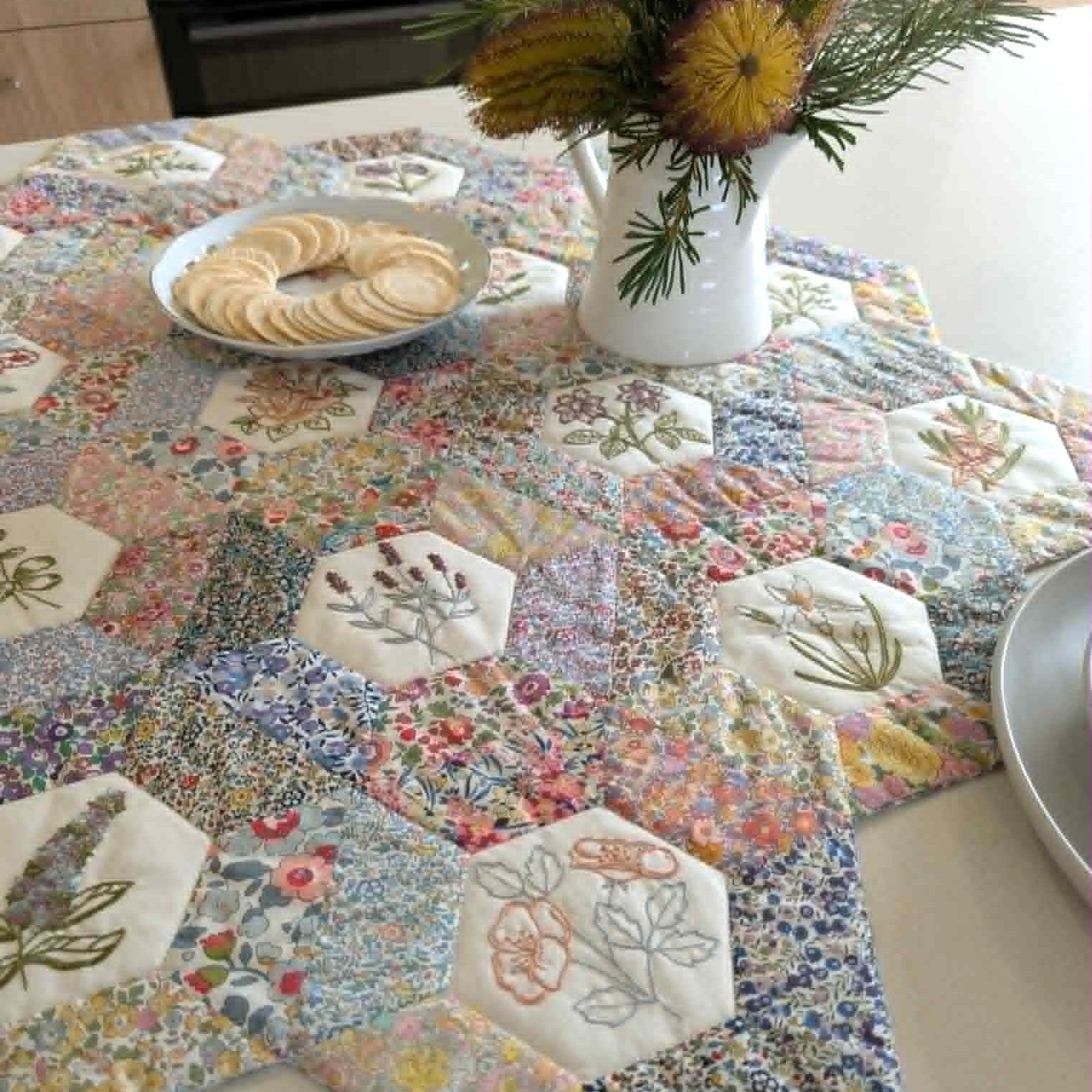 Quilted table runner with floral and geometric patterns on a table.