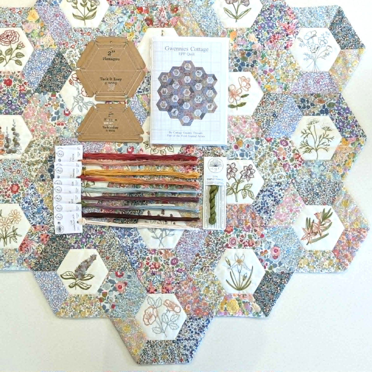Hexagonal fabric samples with floral patterns and sewing tools and embroidery threads on a white background