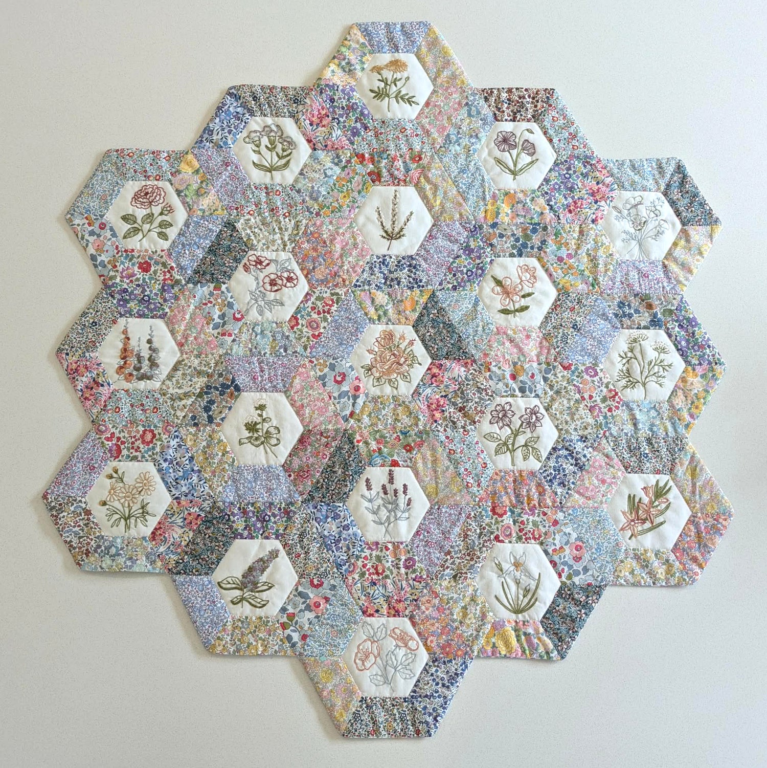 Hexagonal patchwork quilt with floral and nature-themed fabric pieces on a light background