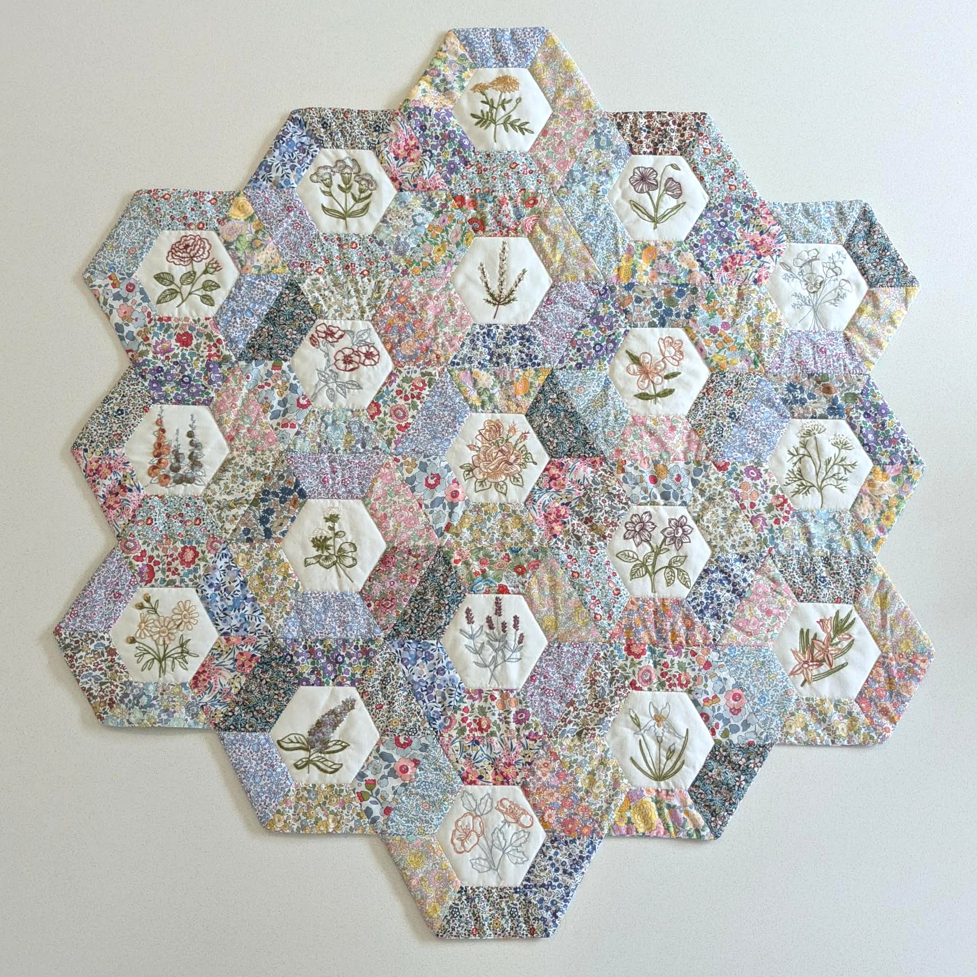 Hexagonal patchwork quilt with floral and nature-themed fabric pieces on a light background