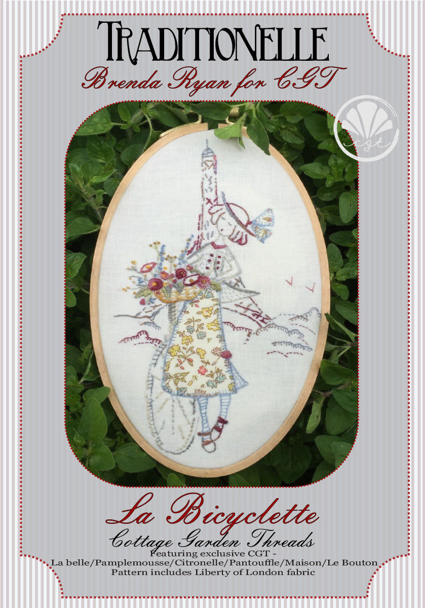 Picture of an embroidery pattern with a young woman in a floral dress holding a basket of flowers next to a bicycle in front of the Eiffel Tower.