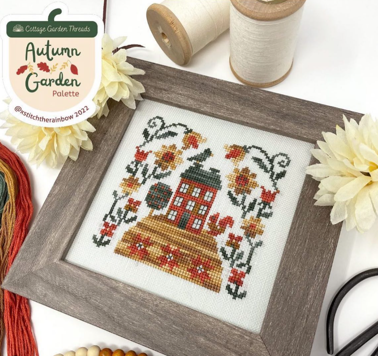 Cross-stitch using Autumn garden palette of house on a hill with flower border