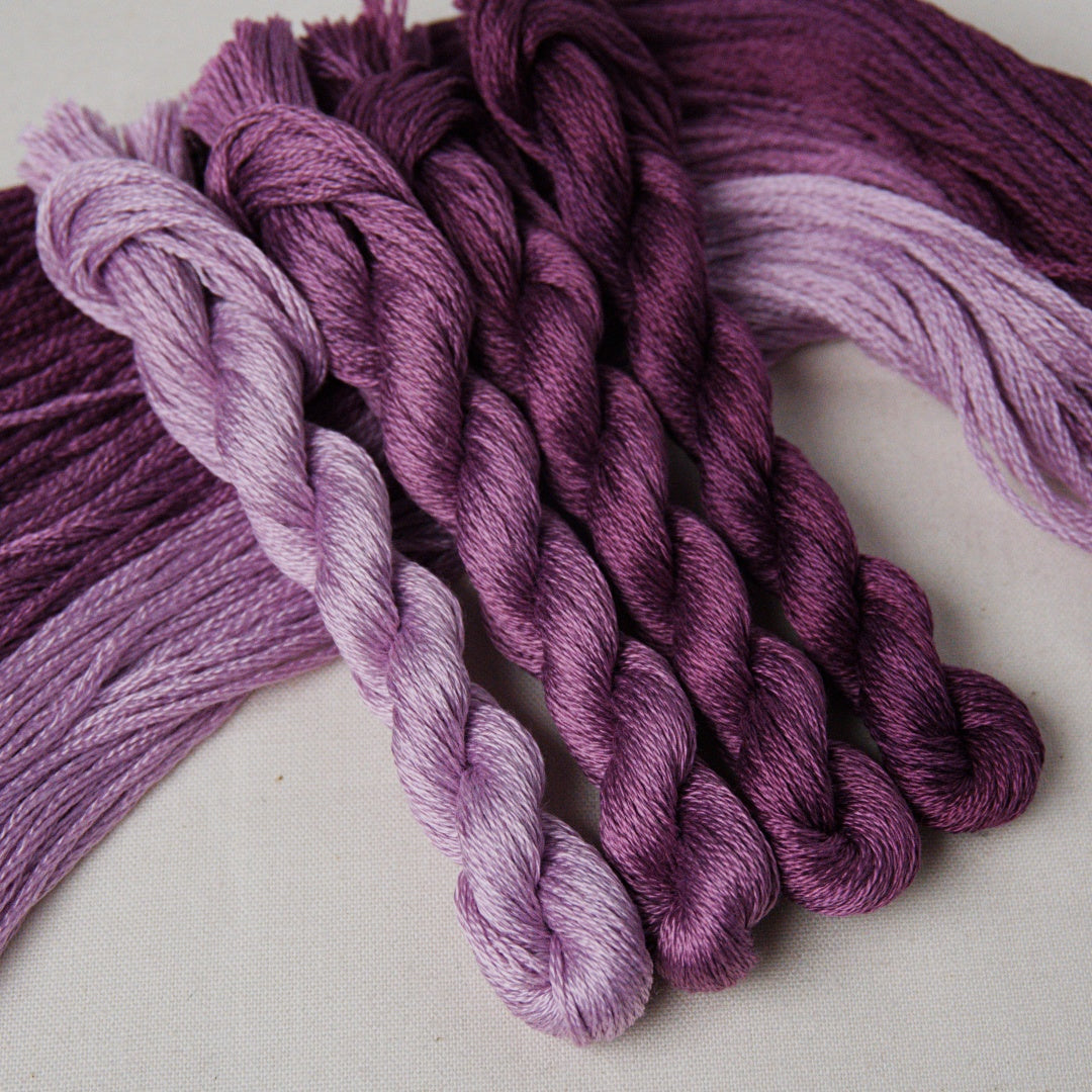 Several twisted skeins of embroidery thread in shades of purple and lavender.